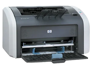 Na zdjęciu widoczna jest drukarka HP LaserJet 1010 w klasycznym, czarnym kolorze. Urządzenie stoi na biurku, gotowe do pracy, z podłączonym kablem USB do komputera. Widać panel sterowania z przyciskami włączania i gotowości. Drukarka prezentuje się schludnie i kompaktowo, idealna do domu lub małego biura.